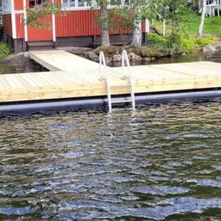 Putkiponttonilaituri T‑malli, jossa penkit ja kävelysilta; ruskea kestopuu ja ketjut rantakiinnityksessä.