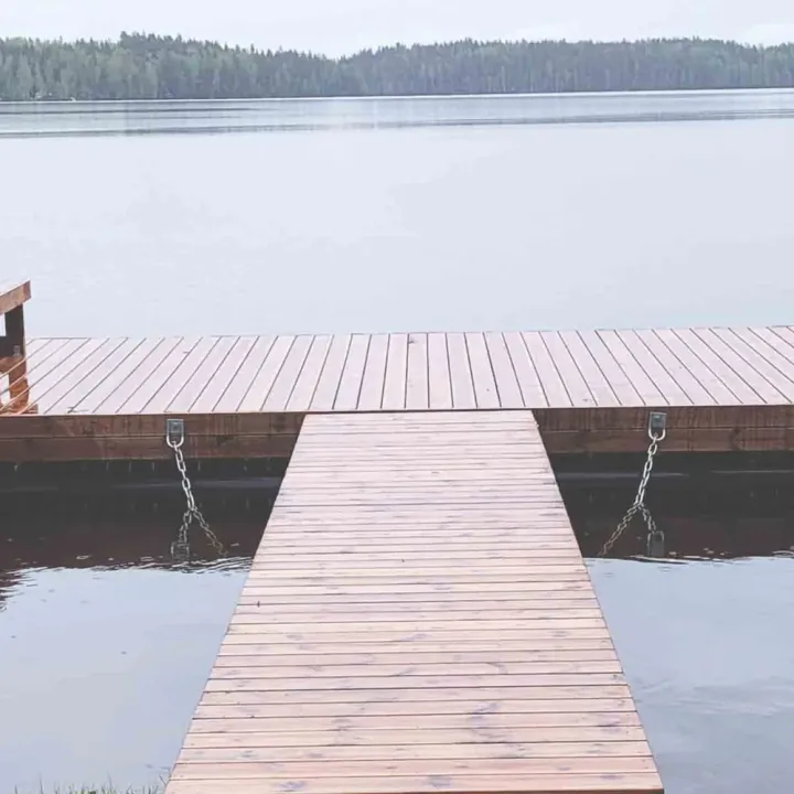 T‑mallinen putkiponttonilaituri mökin edustalla; leveä kansiosa, kävelysilta ja uimaportaat.